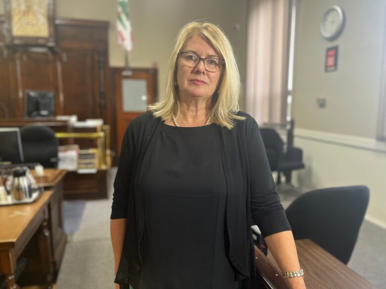 A woman in a black dress stands in a courtroom. 