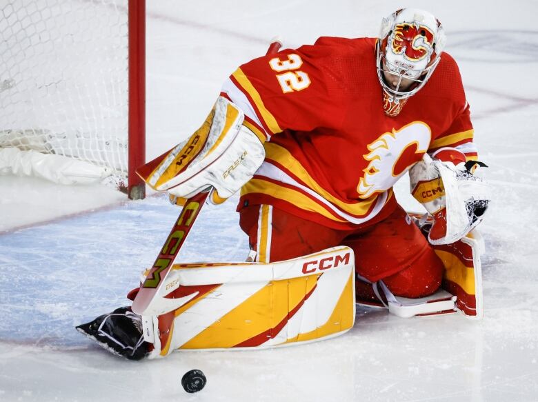 A hockey goalie wearing red and yellow saves a puck from going into the net.