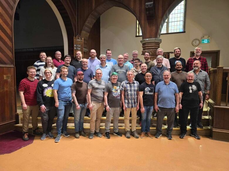 Three rows of men standing in a church building, looking at the camera for a group picture.