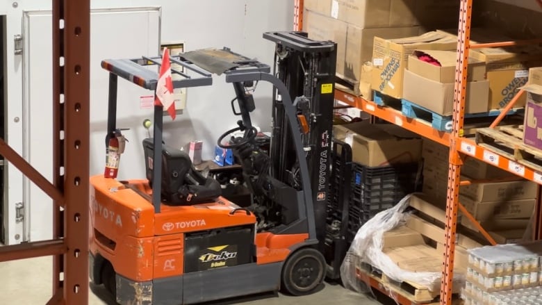 A machine sits idle beside large shelves with boxes of clothes and canned food. 