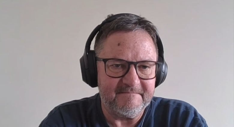 A man wearing a headset looks intensely into the camera