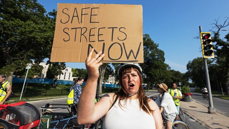 A person wearing a bike helmet stands holding a sign that says 