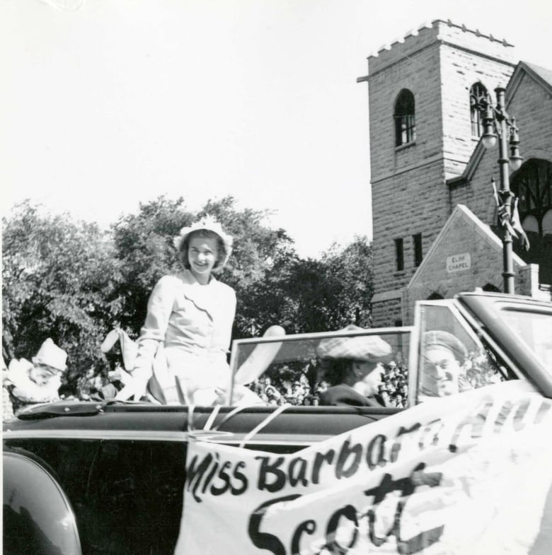 Black and white photo of a woman in a convertible car as part of a parade