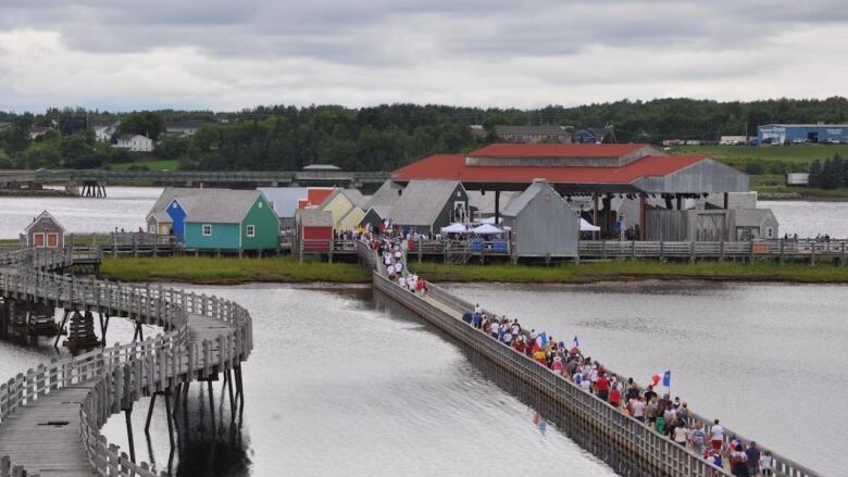 A line of people wearing colourful clothing walk across a wooden bridge.