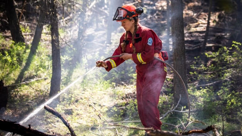 A woman in a red fire suit sprays water in a forest