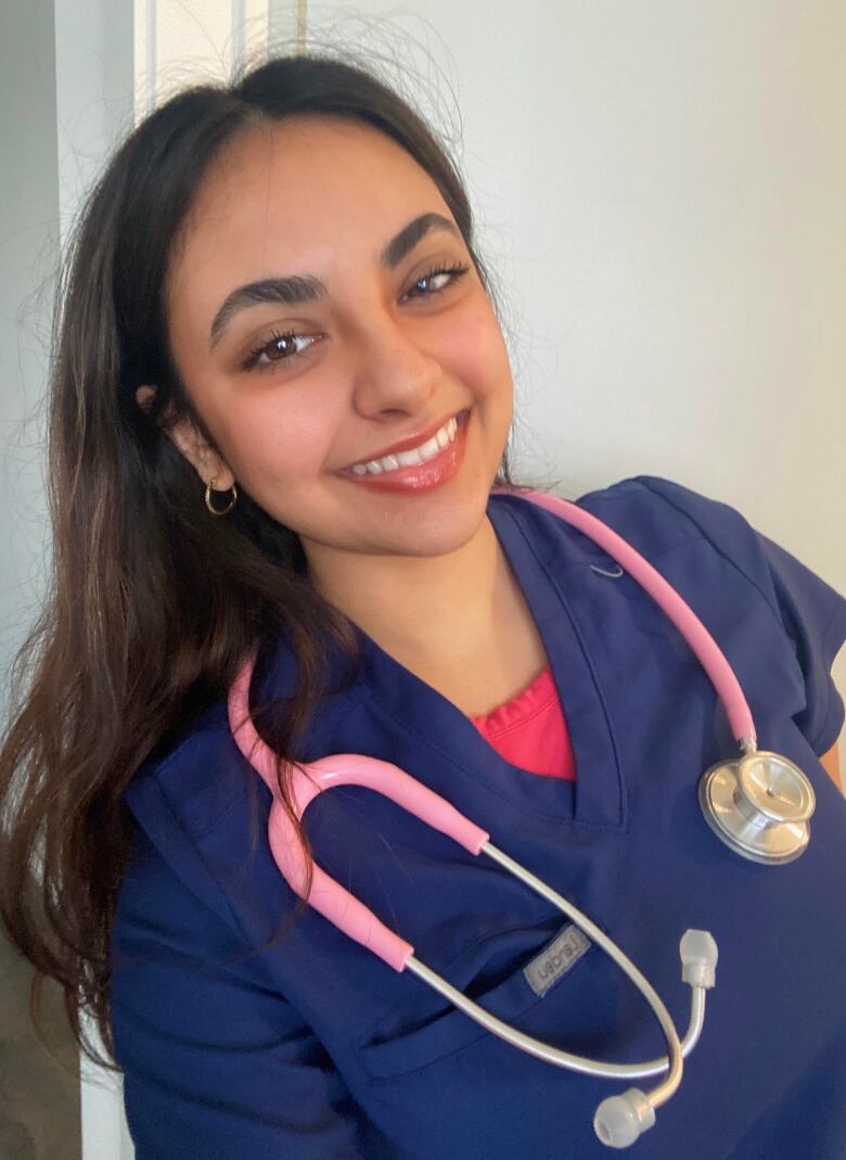 A selfie of a woman wearing blue scrubs with a pink stethoscope around her neck. 