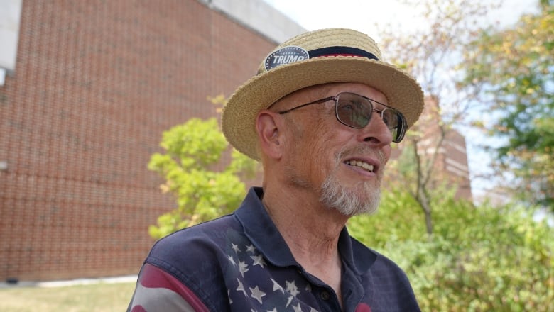 A man in a shirt printed with the American flag sits on a lawn chair in front of a red brick building.