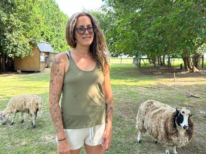 A woman standing in an outdoor area with two sheep in the background.