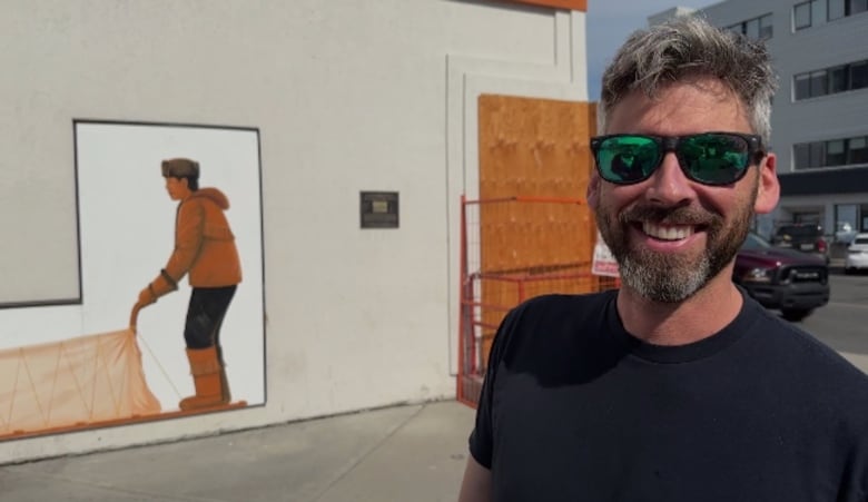 A man smiles in front of a building with a dogsled painted on it.