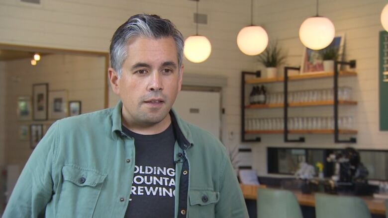 A man with grey and black hair stands in a restaurant with white, wood, black and pistachio decor. 