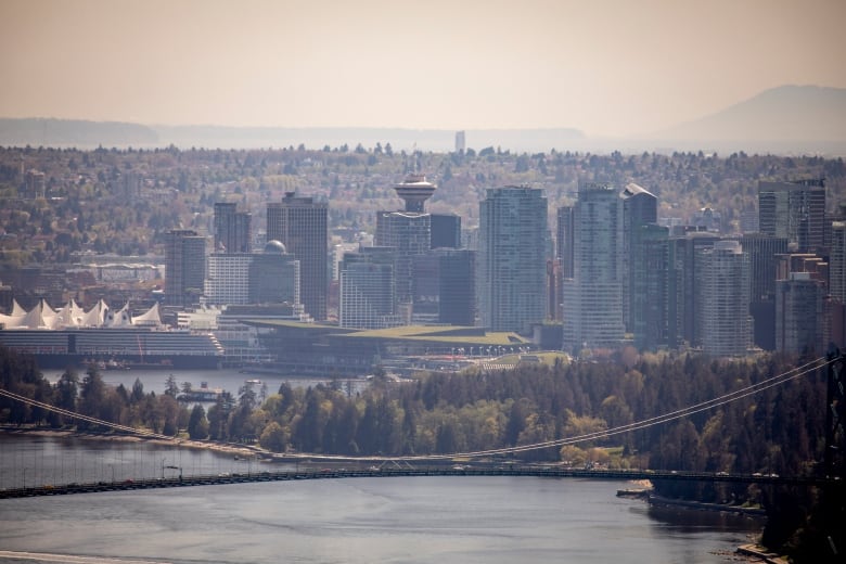 A city's downtown is pictured on a hazy day, with skyscrapers visible in front of a large number of trees.