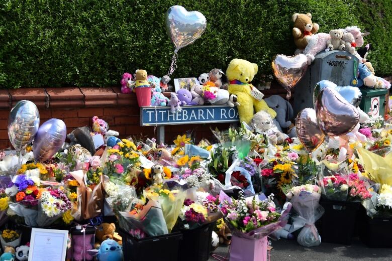 A huge pile flowers, balloons and stuffed toys.