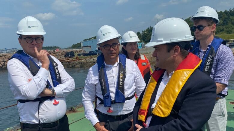 A group of people in hard hats stand on a barge. 