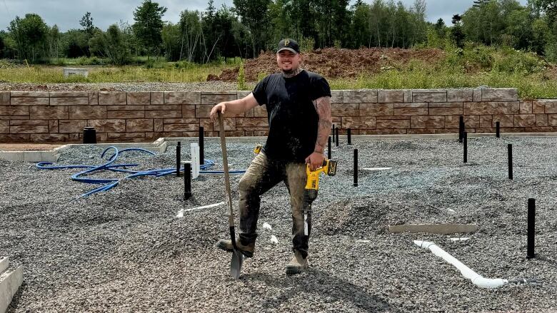 A man stands in a gravel while holding a yellow power tool.