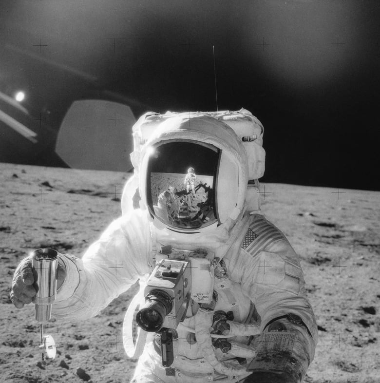 A black-and-white image of an astronaut on the moon holding a silver container.