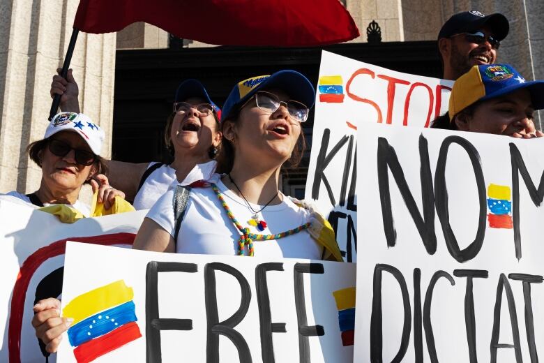 A group of protestors stand outside a building holding signs in support of Venezuela. 