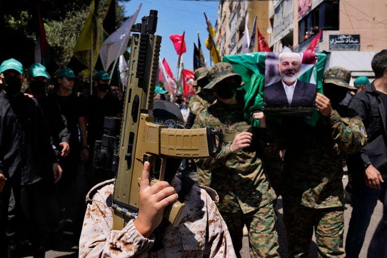 Boy with face covered holds toy gun surrounded by crowd of people.