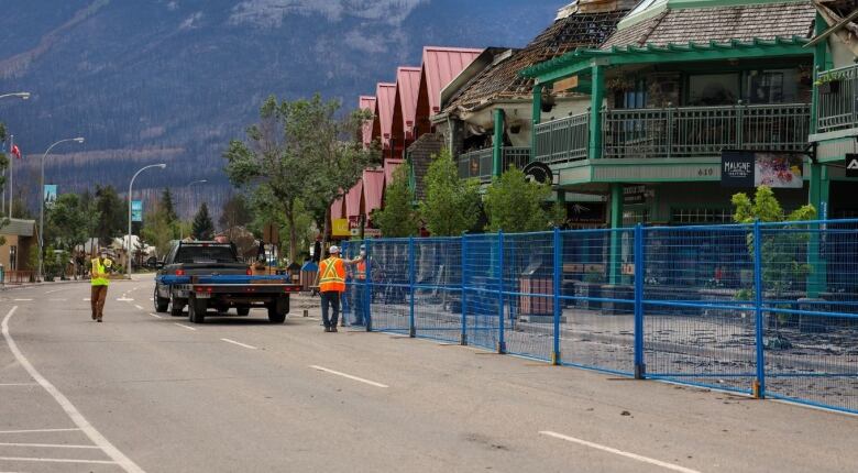 Perimeter fencing is set up around fire-damaged businesses on a street. 