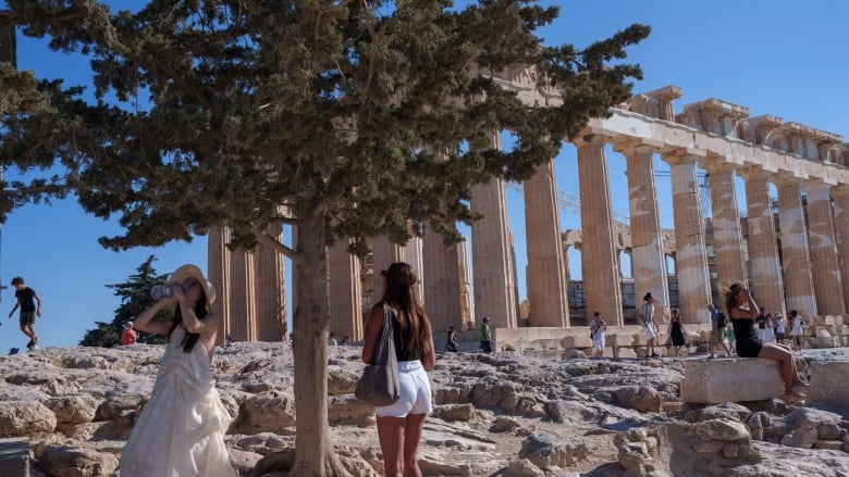 A woman drinks water in front of the ancient Parthenon Temple during a hot, windy day at Acropolis hill , in Athens, in July.