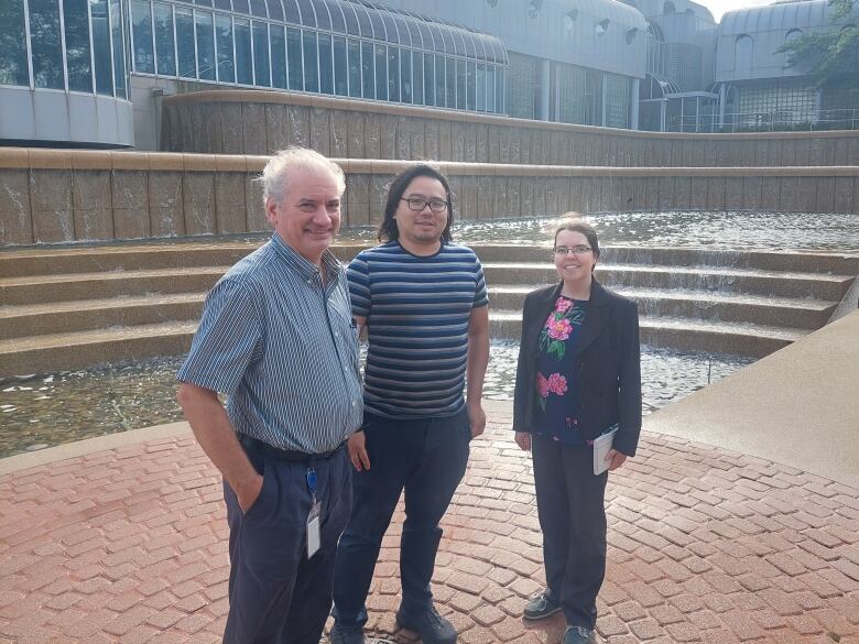 Three people standing side by side in front of a water fountain.