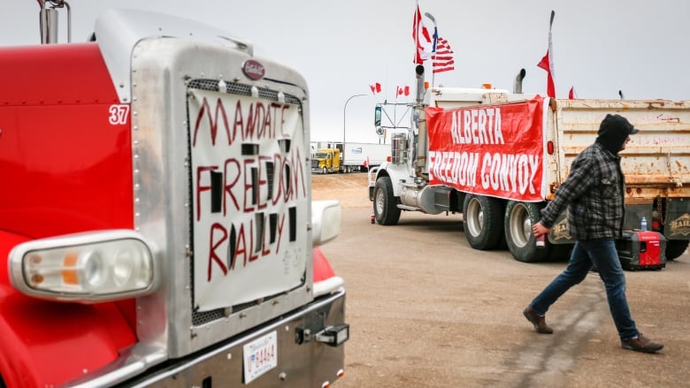 A person can be seen walking by two trucks at a protest. On one of the trucks it says mandate freedom rally.