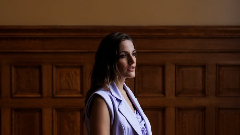 A woman is pictured in front of a wood-paneled wall.