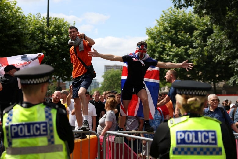 Demonstrators stand on a structure and gesture as police look on.