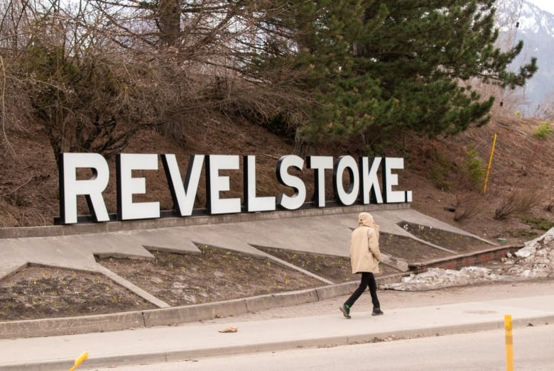 A person walks by a large sign that reads 'Revelstoke.'