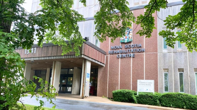 A grey and brown building with an awning and green plants around it.