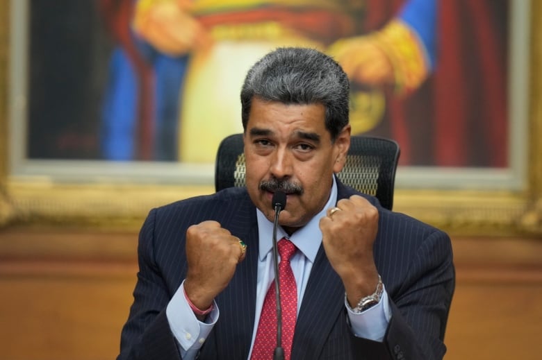 A person gestures by holding up their fists while speaking into a microphone.