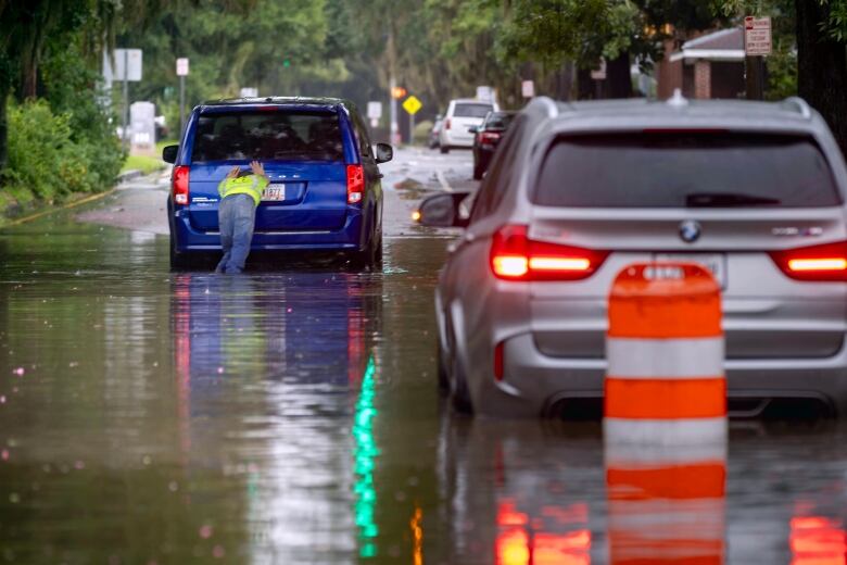 A man pushes his stranded vehicle along a flooded street after heavy rain from tropical storm Debby.