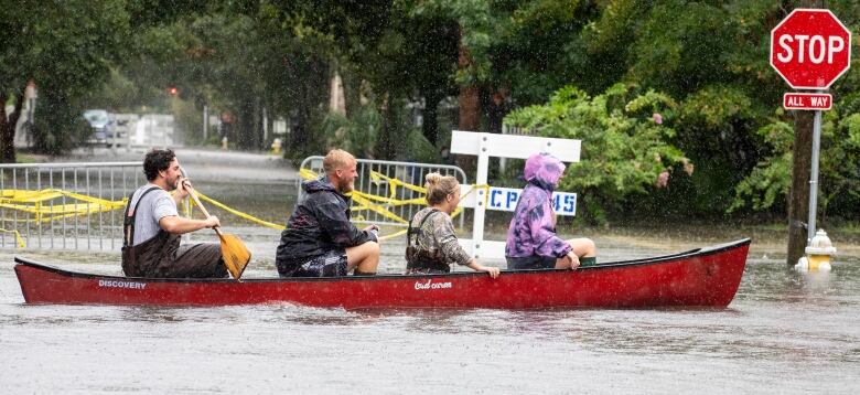 Four people paddle on a canoe on a flooded street.