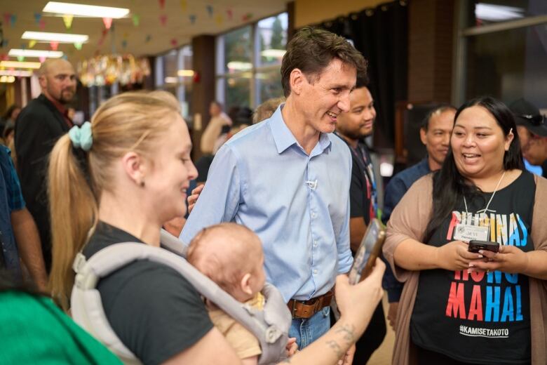 A man wearing a blue button down shirt greets people at an event. 