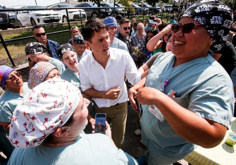 A group of doctors, nurses and a man in a dress shirt gather at a picnic table during a barbecue. 