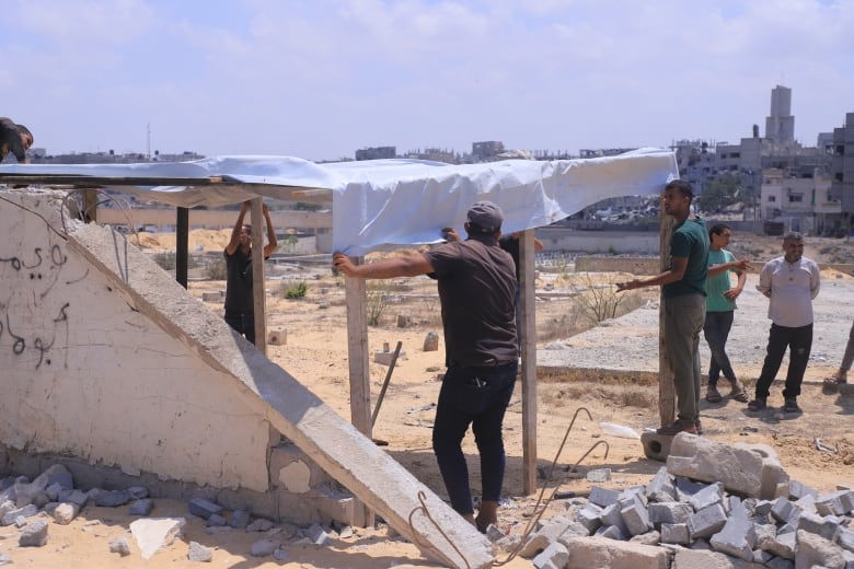 A man in a brown shirt and black pants pulls a white nylon tarp over a wood structure in a cemetery