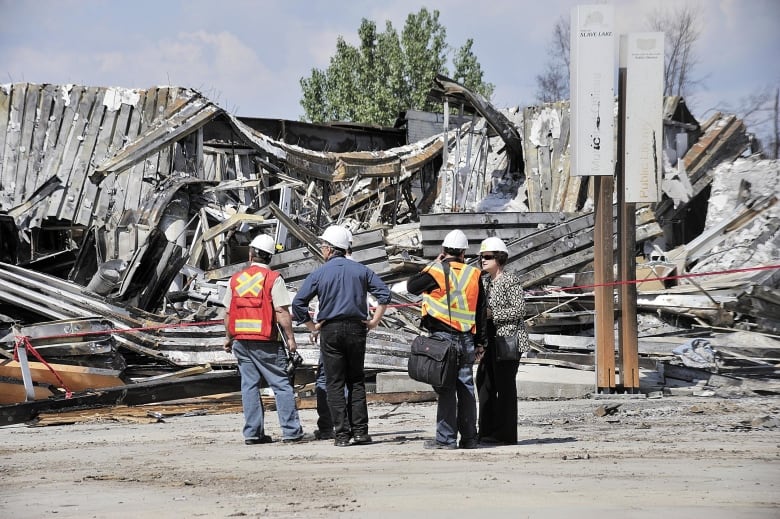 Men and women in construction helmets stand in front of collapsed buildings. 