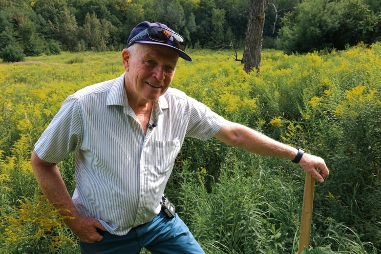 Man stands in field with hand on wooden post