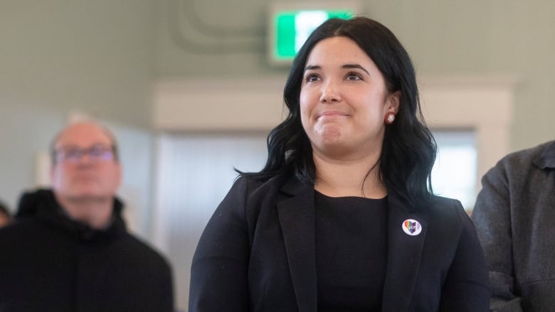 A woman stands with her hands folded.