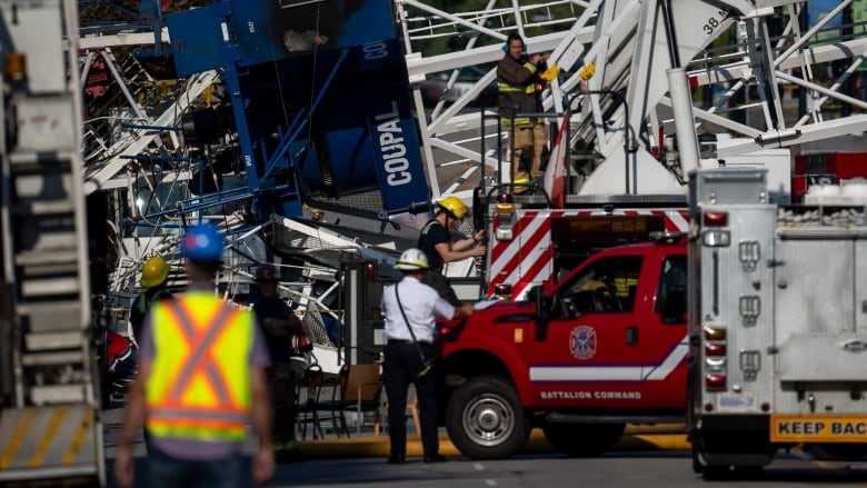 Firefighters approach a crane that's fallen across a street. 