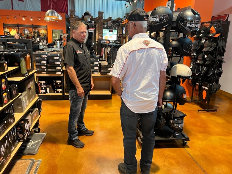 Employee in motorcycle shop helps customer by rack of helmets