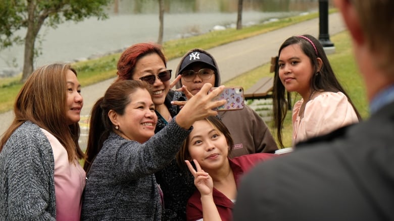 A group of women are seen posing with a mobile camera for a selfie.