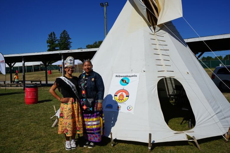 Two women standing beside a tipi.