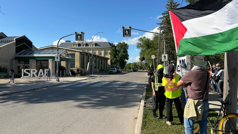 Protestors wave Palestinian flags and hold signs outside. 