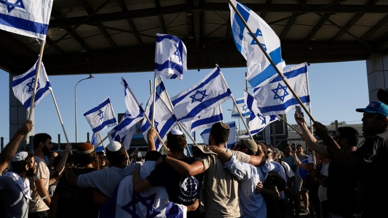 A group congregates, waving more than a dozen Israeli flags.