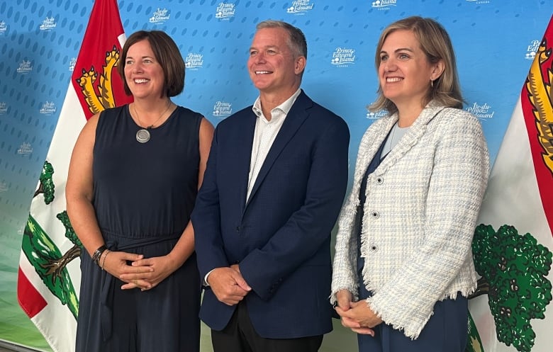 Two women and a man stand in front of a Prince Edward Island flag.