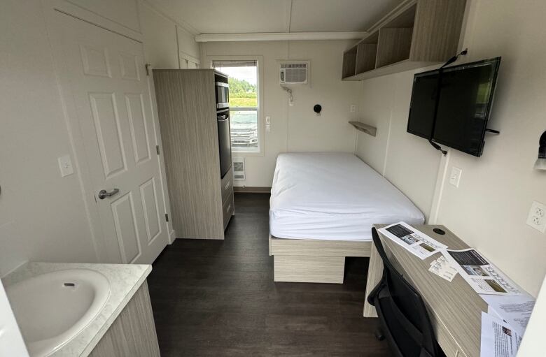 Inside of a trailer with hardwood floor, bed, television mounted to wall, and dresser. 