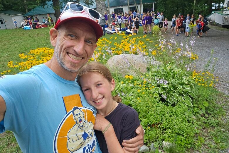 A man poses with a young girl. A group of kids are in the background.