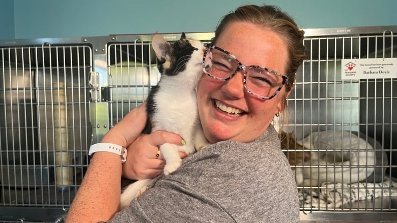 A woman holds a small kitten close to her face as the kitten licks her cheek and she smiles.