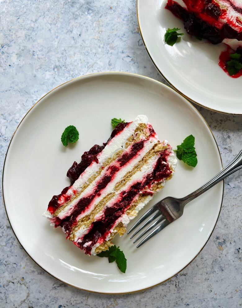 A cross section shot of a cake with layers of graham craker, whipped cream and sour cherry sauce.