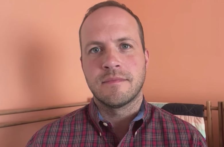 A man in a plaid shirt stares into the camera before a Zoom interview begins.